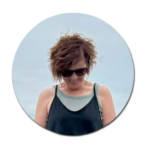 Woman with short curly hair and sunglasses smiling gently.