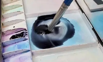 A paintbrush swirls black watercolor paint on a palette, surrounded by various pastel shades. The scene suggests creativity and calmness.