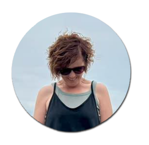 Woman with short curly hair and sunglasses smiling gently.