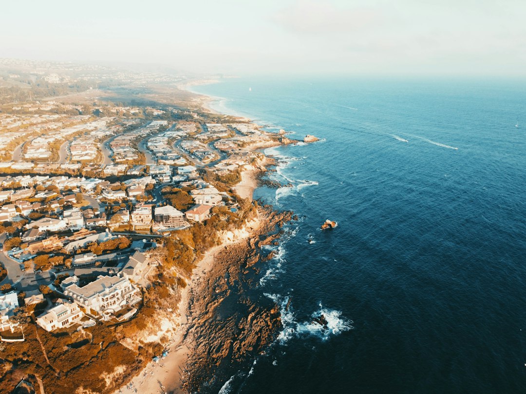Aerial view of a Southern California coastal neighborhood of homes along rocky bluffs with surf breaking below.
