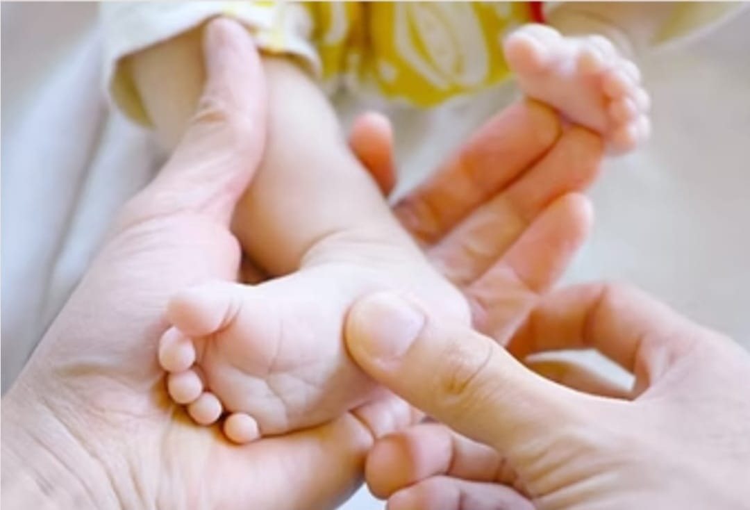 Des pieds de bébé tenus avec douceur dans les mains d'un adulte