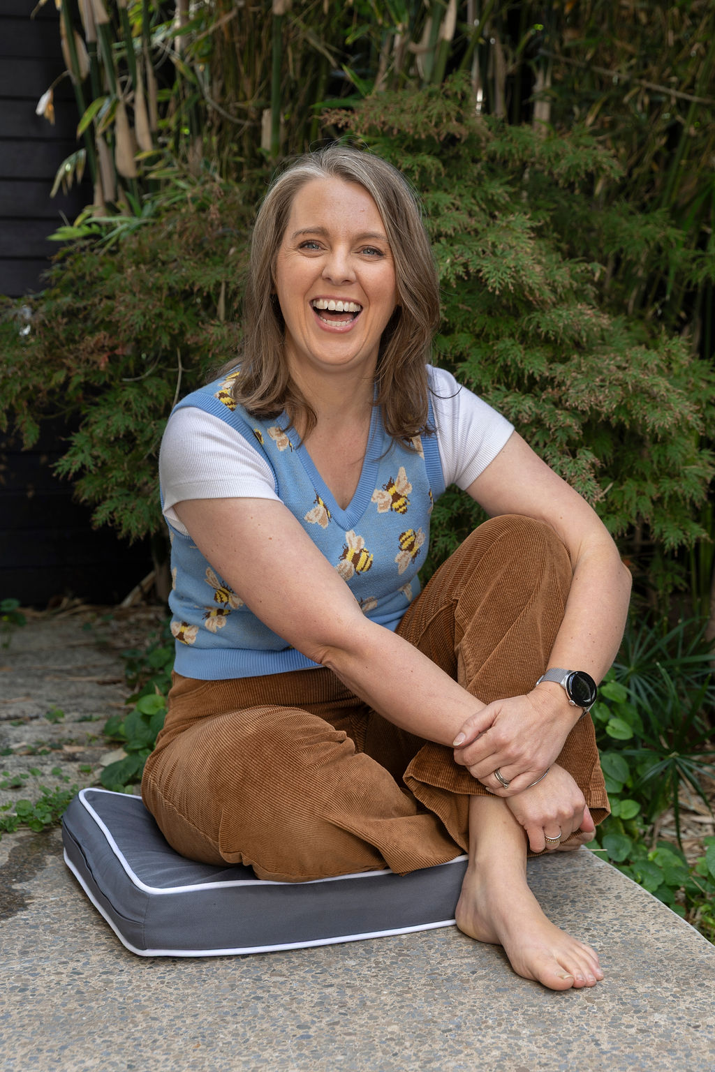 Selena Woodward laughing, sitting cross-legged on a cushion in her garden