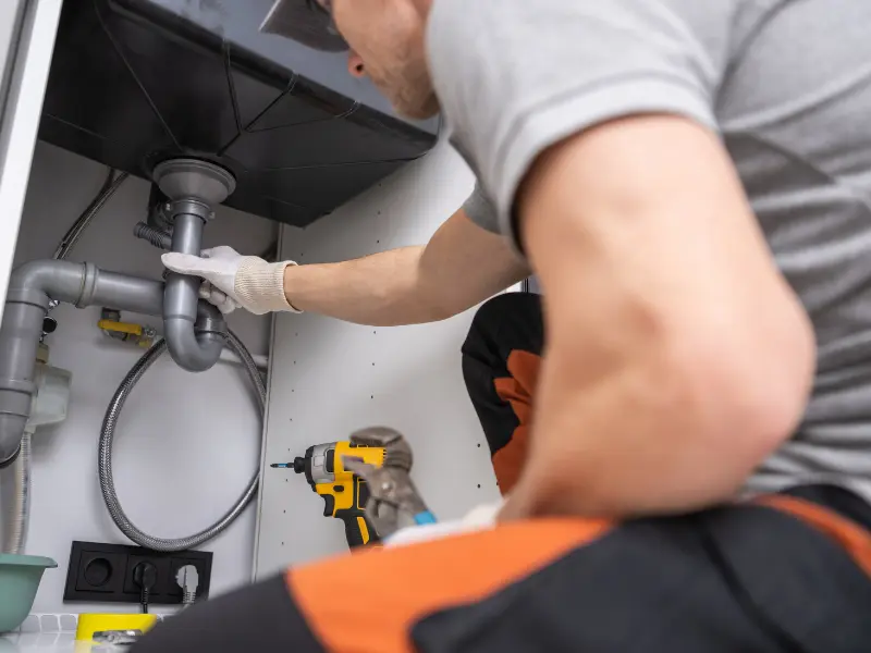 Plumber wearing gloves repairing pipes under a kitchen sink. Plumber wearing gloves repairing pipes under a kitchen sink.