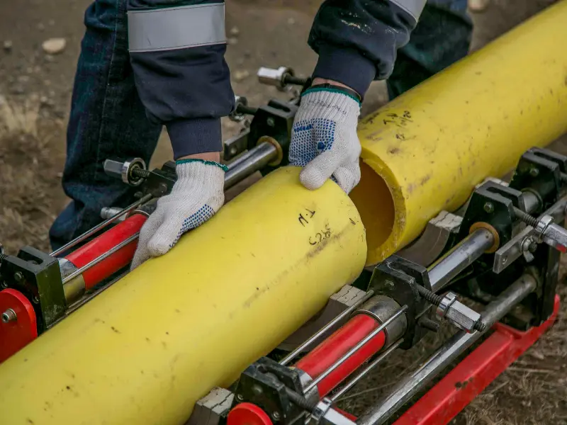 Plumbers fusing a yellow gas pipe together using a pipe fusion machine on a job site.