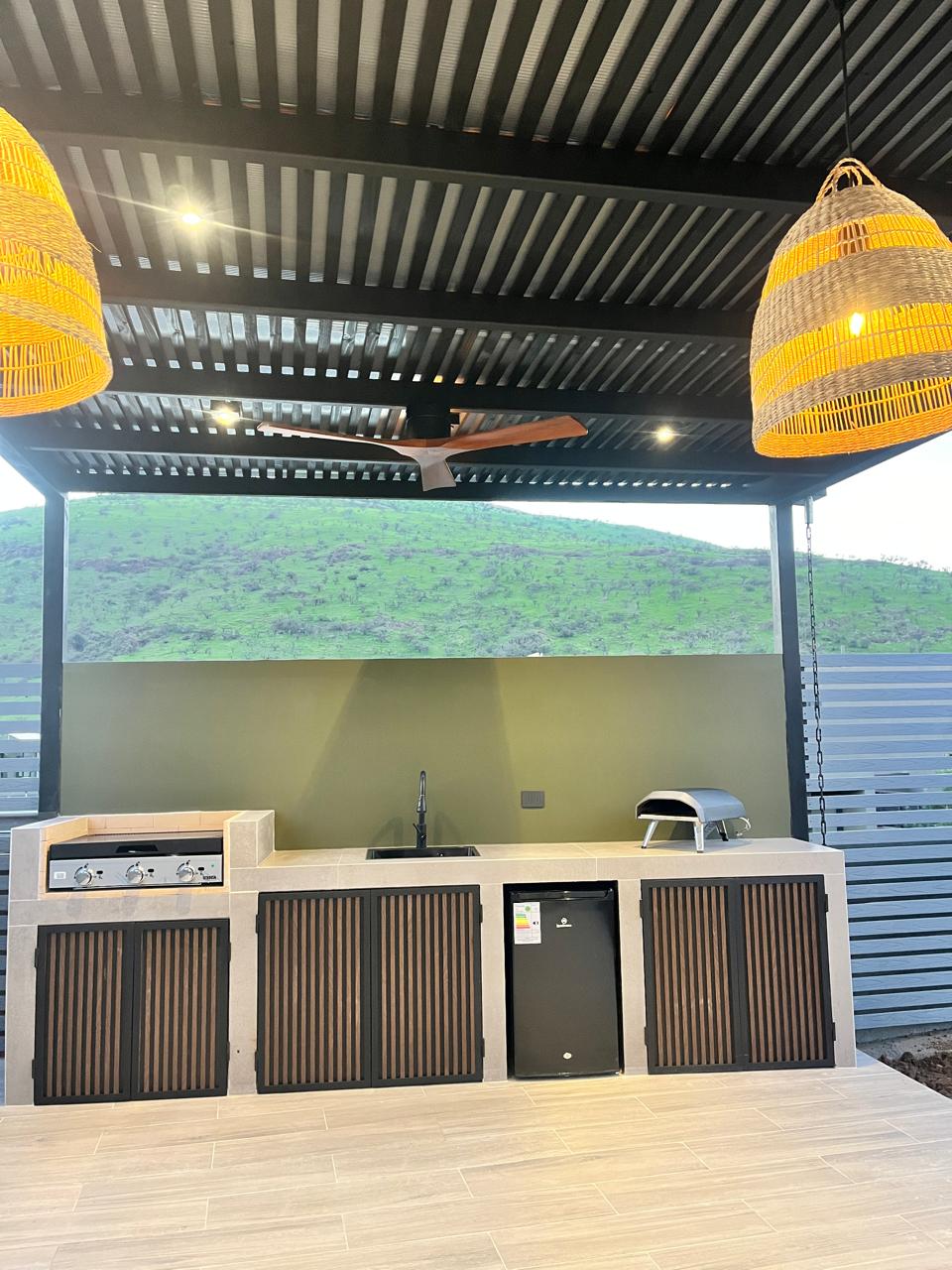 Terraza con pérgola metálica, piso tipo madera y cocina exterior