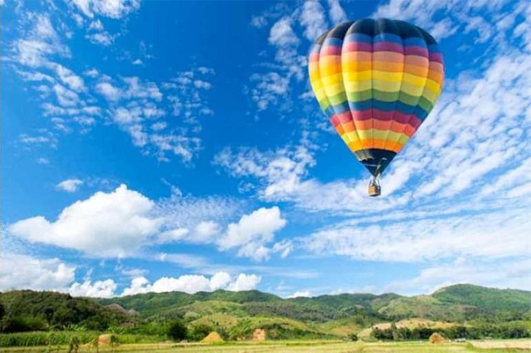 A striped hot-air balloon floating over green hills under a blue sky