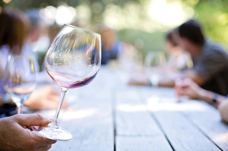 A glass of red wine held up at a long outdoor tasting table