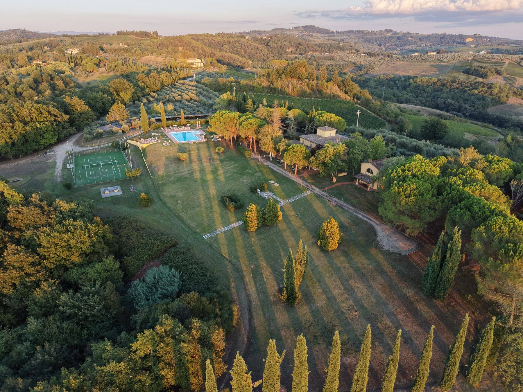 The estate from the air in late golden light, the pool, tennis court and long lawn lined with cypress trees, with the Tuscan hills behind