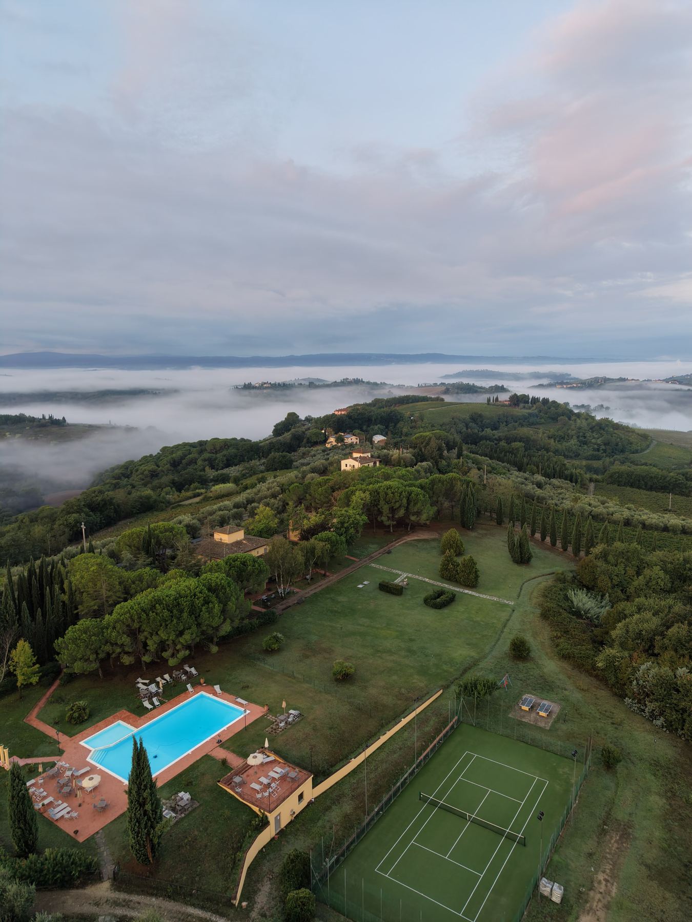 Early morning mist filling the valleys around the estate, with the pool and tennis court in the foreground