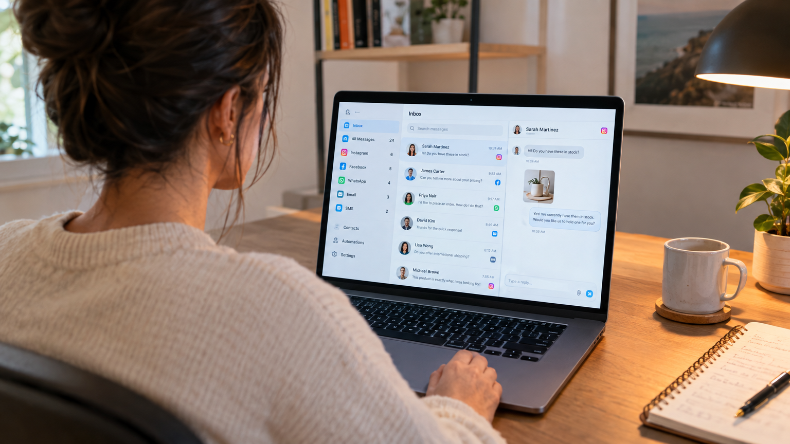 Small business owner at a desk looking at a laptop screen showing a unified messaging dashboard with multiple chat channels