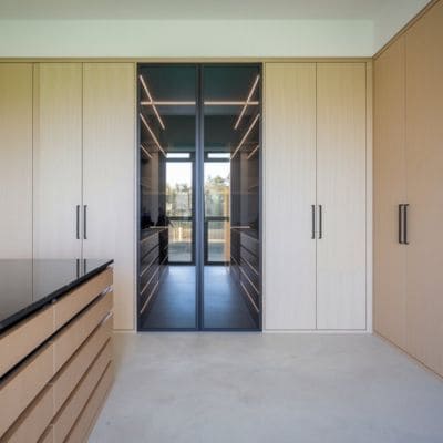 Custom closet with light wood cabinetry and glass doors