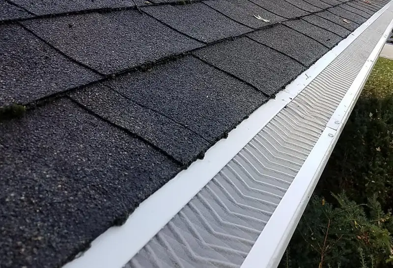 Close view of a gutter guard beneath roof shingles