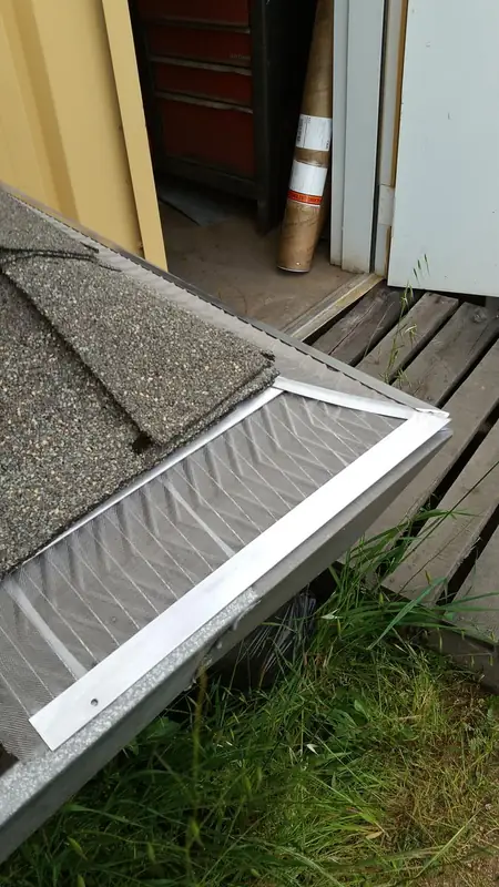 Custom fitted gutter guard section beside roof shingles