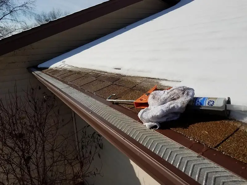 Gutter guard installation in progress beneath a snowy roof