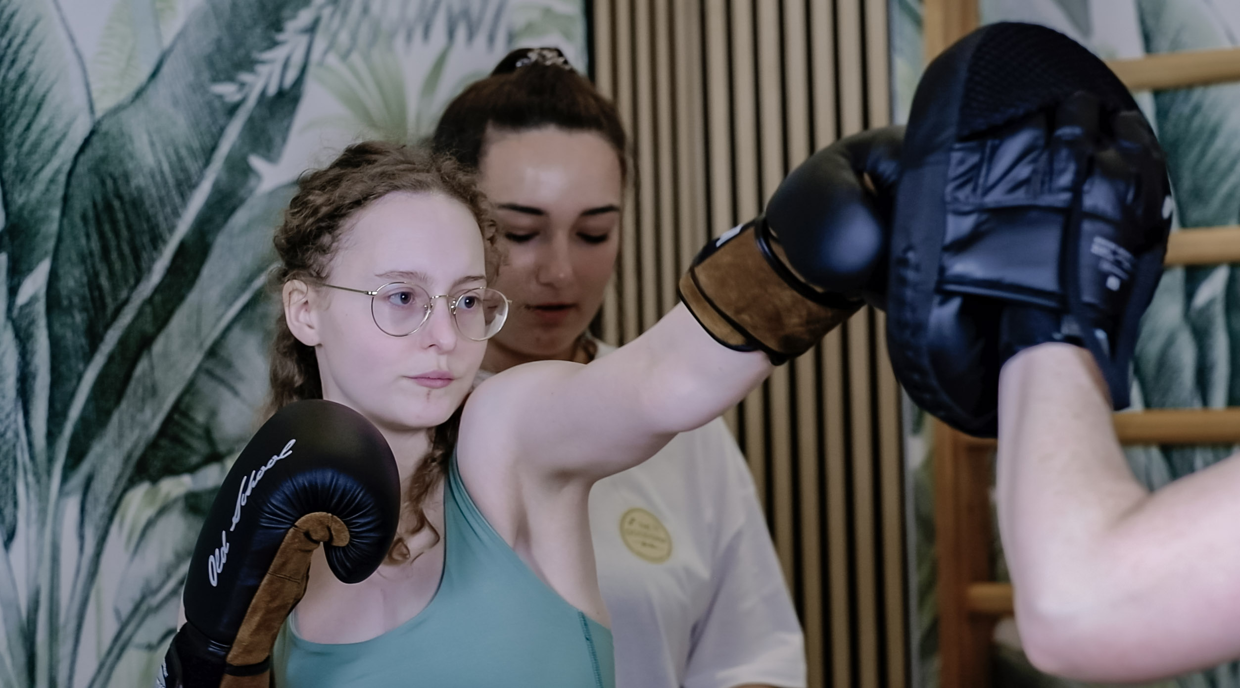 A trainer guiding a woman through a boxing pad drill