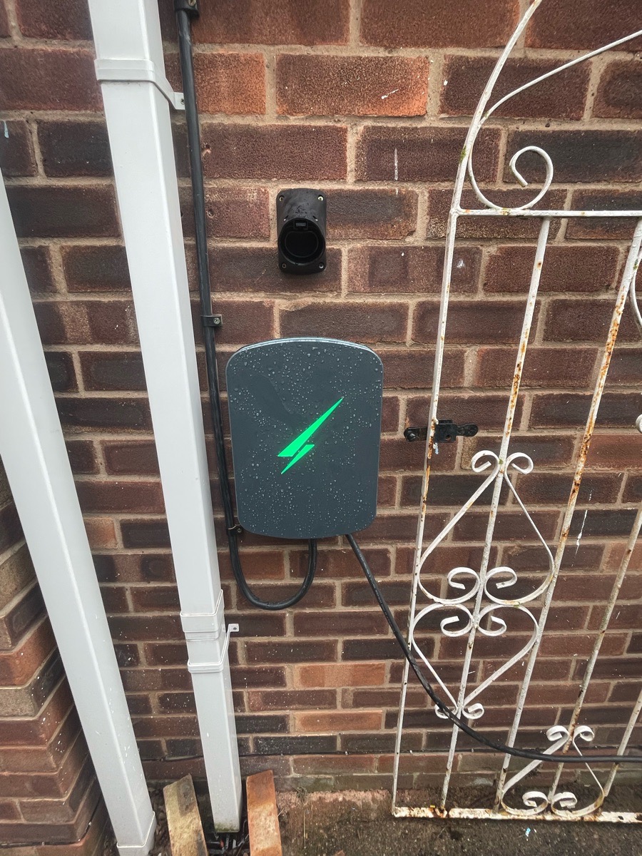 Qualified electrician installing a modern white electric vehicle home charger unit on the exterior wall of a Derby property