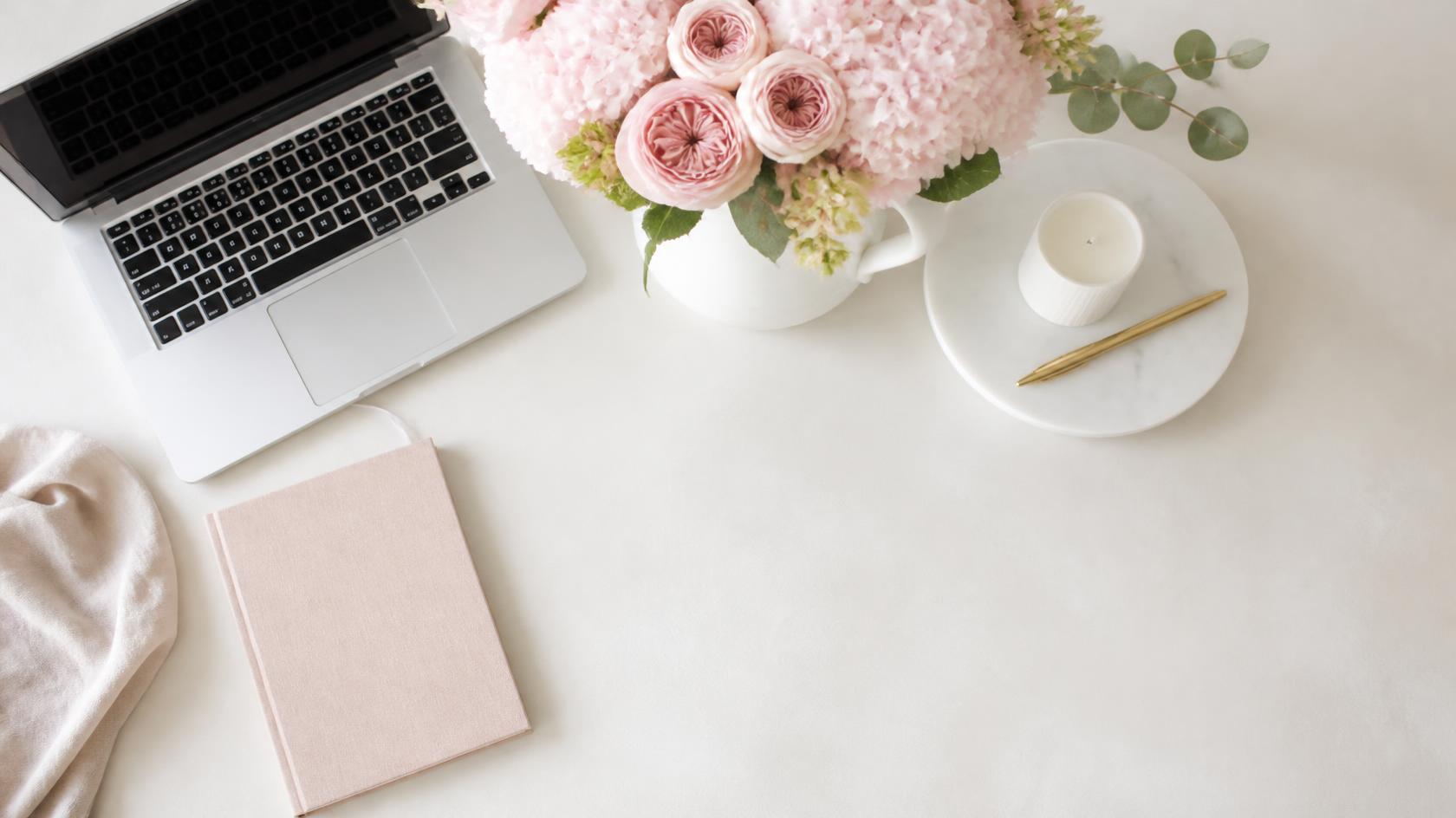 A white desk with a laptop, pink hydrangeas and a notebook