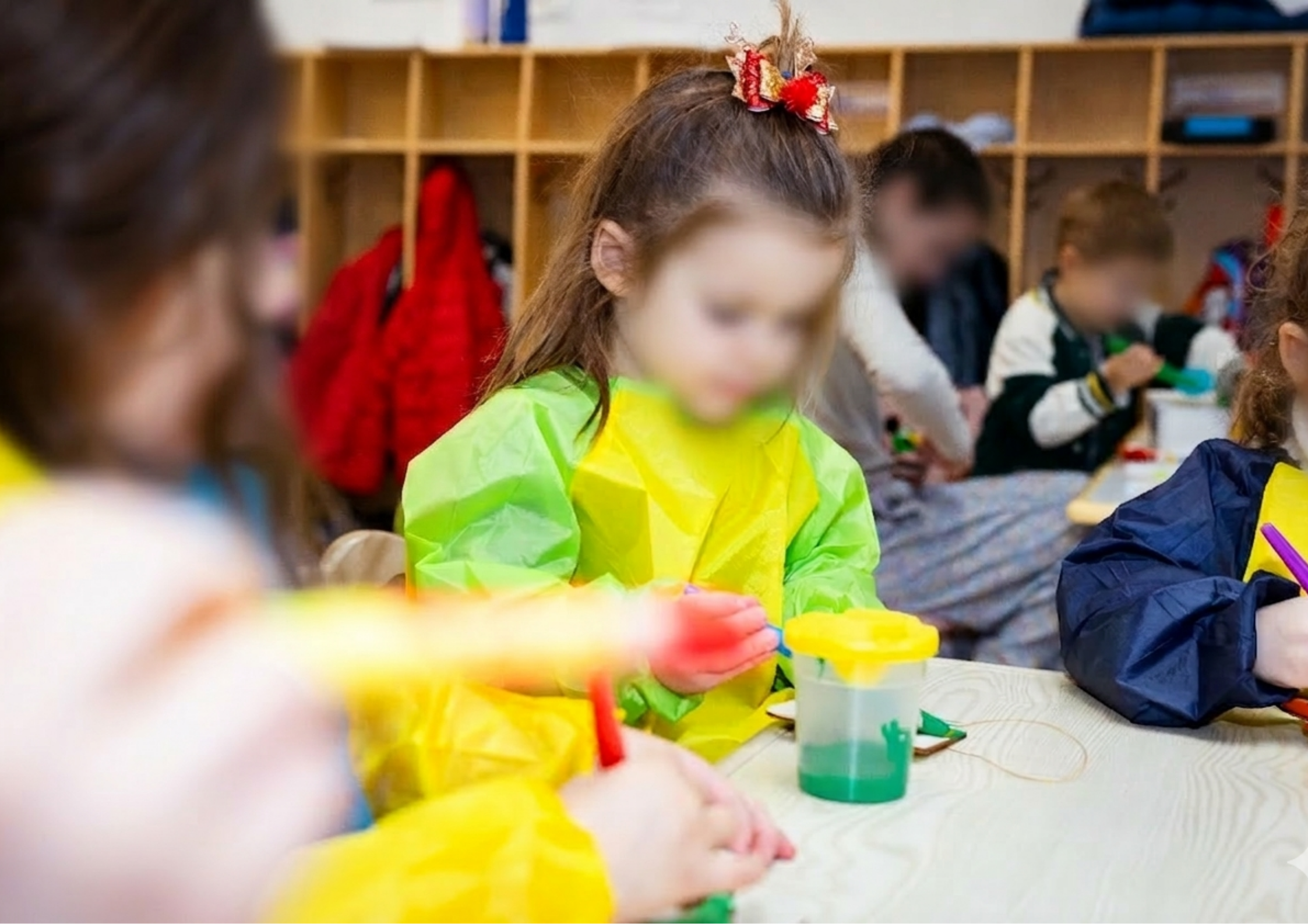 Young children doing arts and crafts activity in a classroom wearing colorful paint smocks