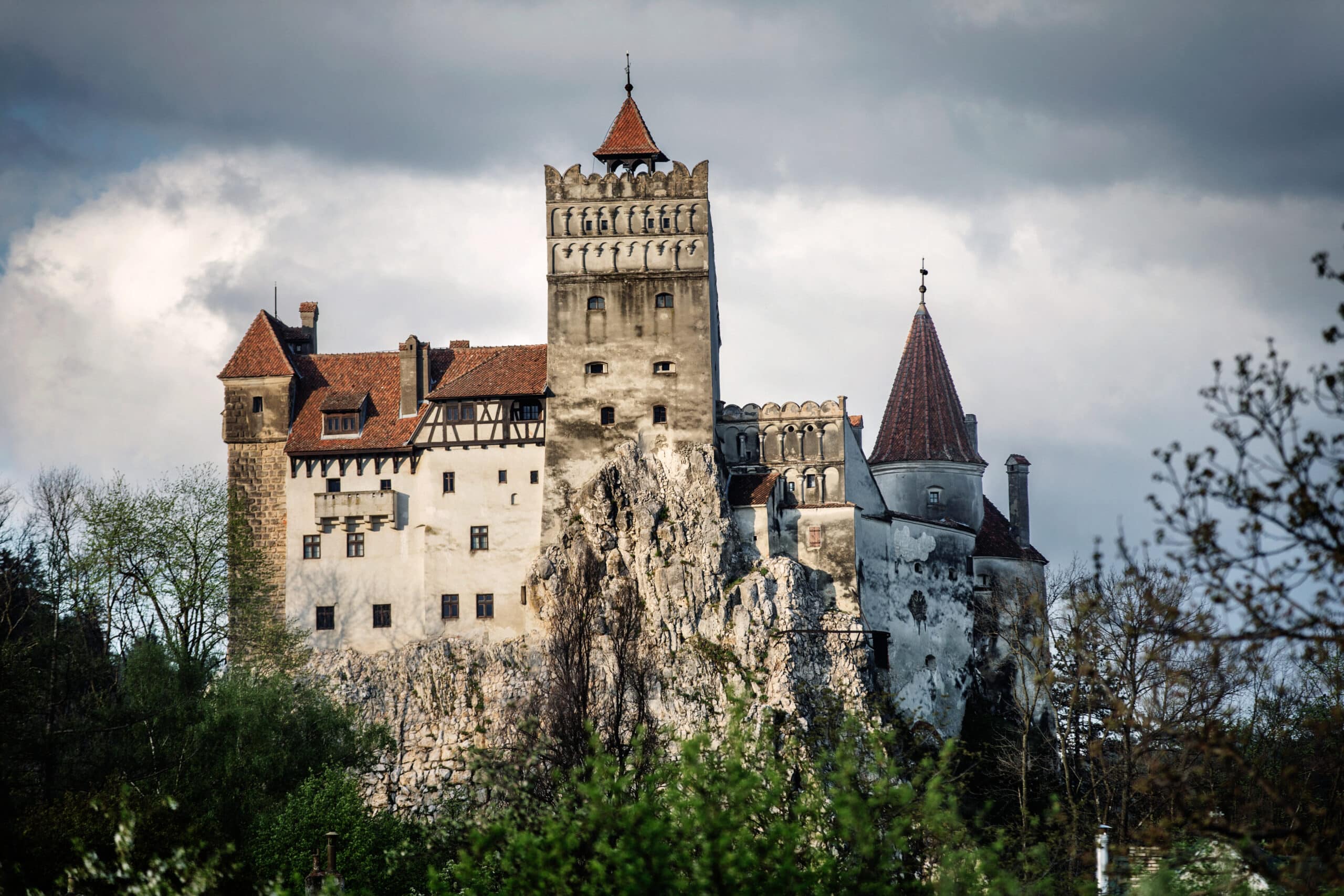 Castelul Bran pe stâncă, cu acoperiș roșu, înconjurat de vegetație