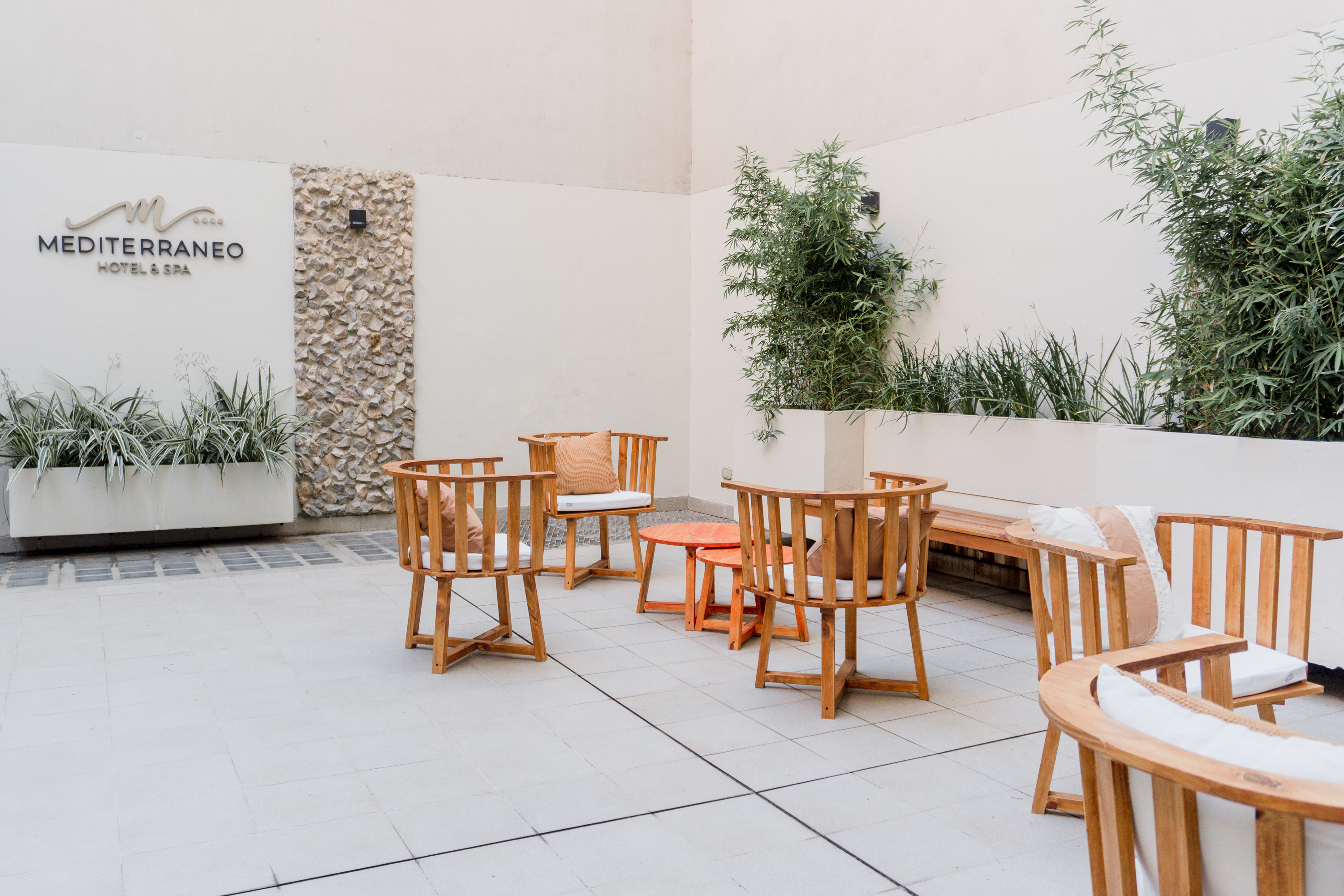 Patio de Mediterráneo Hotel & Spa con sillones de madera y plantas junto al nombre del hotel.