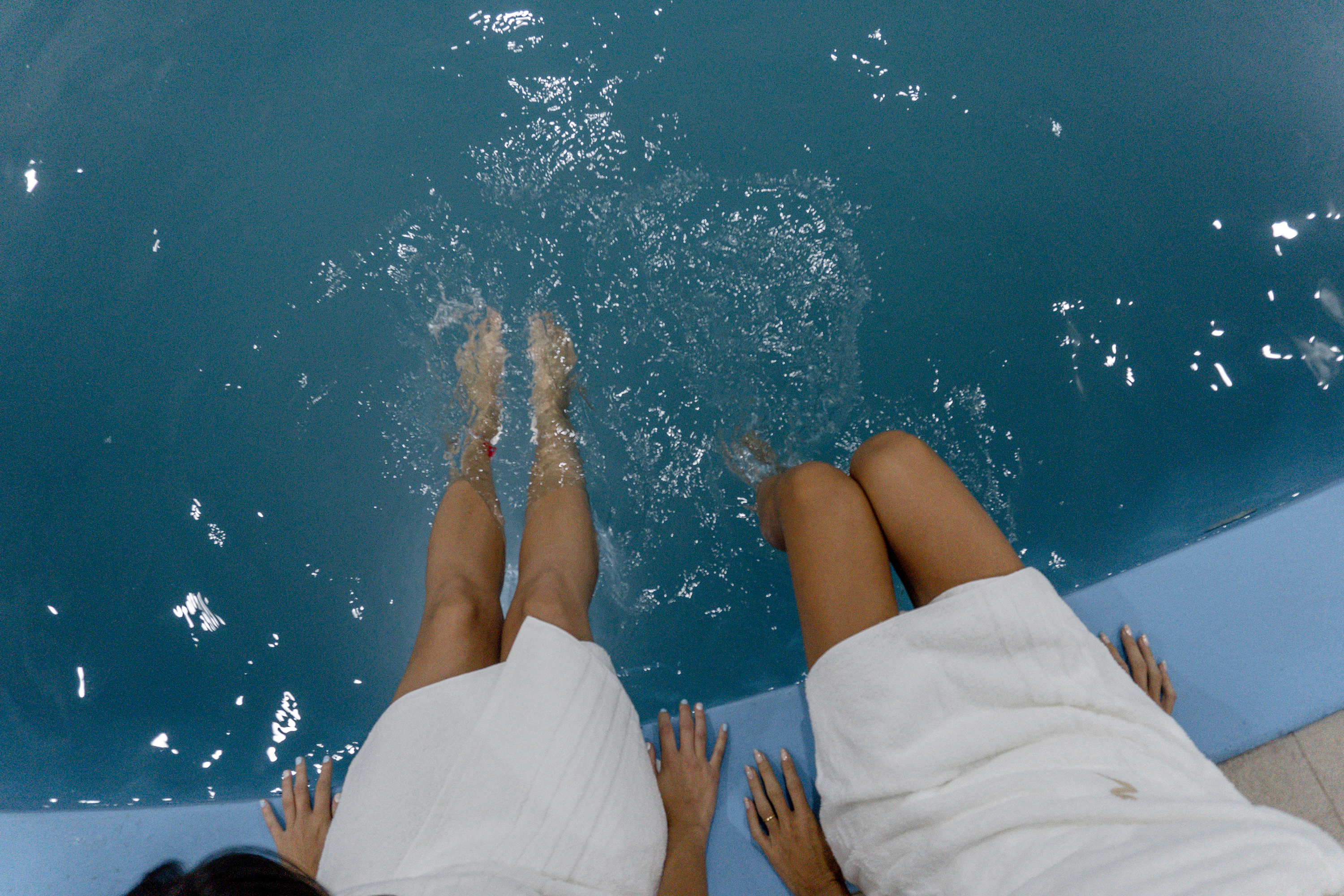 Dos personas con batas descansan al borde de la piscina del spa.