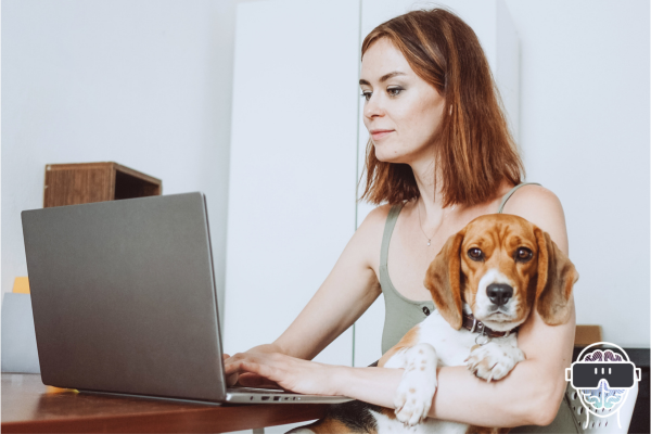 lady sat at a laptop on a table with her beagle dog sat on her knee in her arms