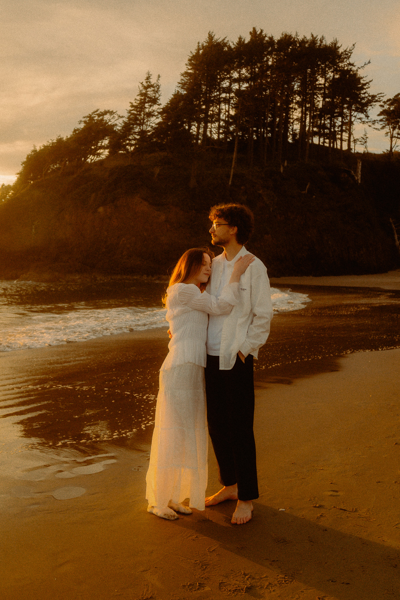 Mark and Sofia embracing on the road as elk graze nearby