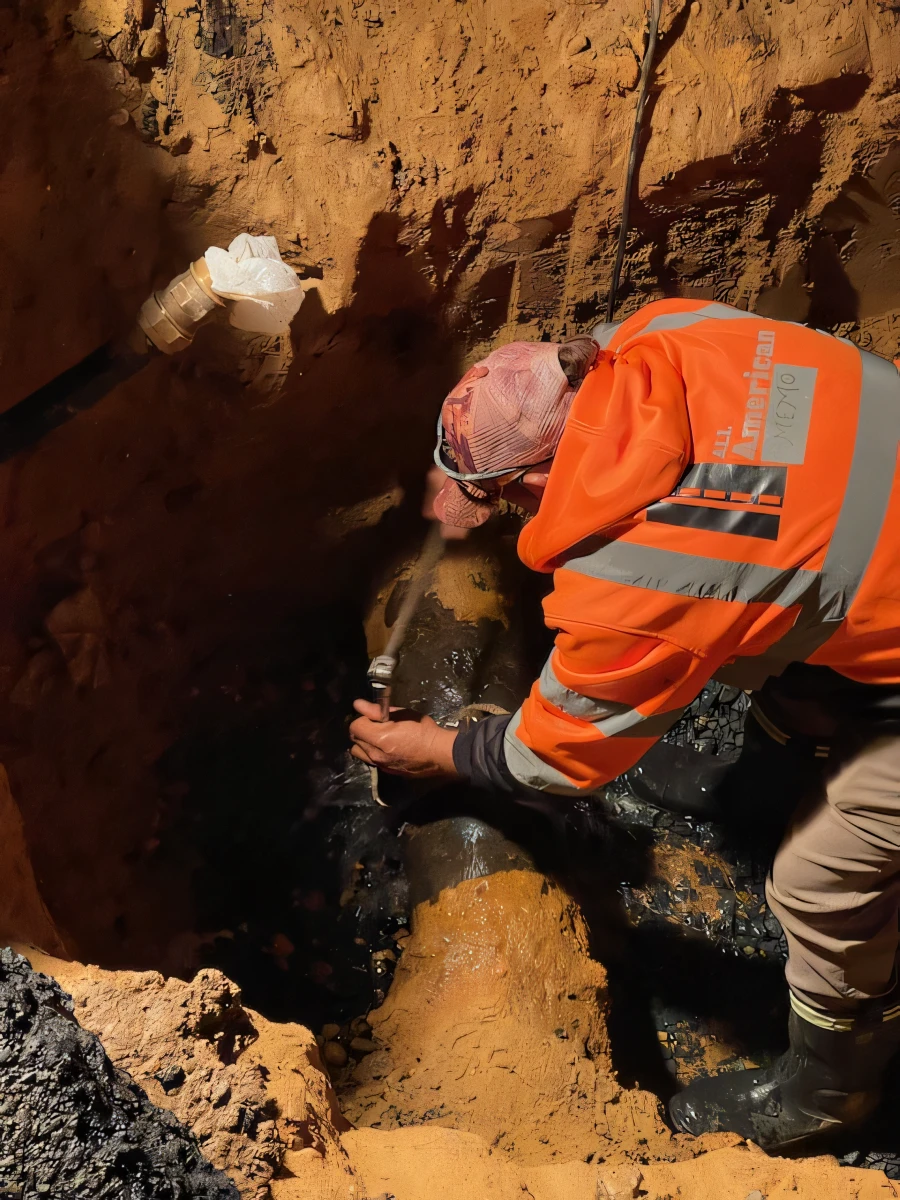 Worker in orange high-visibility jacket repairing an underground pipe in a trench