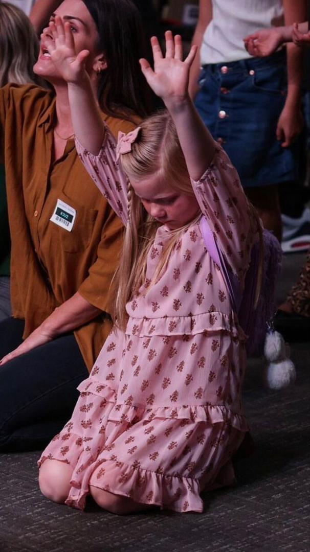 Young girl kneeling in church with hands lifted in worship during a prayer session, expressing faith, devotion, and the power of prayer in a child’s spiritual life.