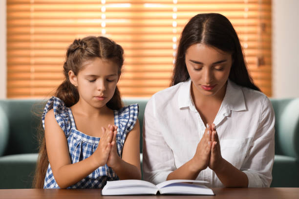 Mother and daughter praying together at home with an open Bible, representing Christian family devotion, faith-filled parenting, and spiritual growth in the home.
