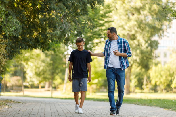 Father walking alongside his teenage son in a park, having a meaningful conversation and building trust through open communication, guidance, and emotional connection in a Christian family. Father walking alongside his teenage son in a park, having a meaningful conversation and building trust through open communication, guidance, and emotional connection in a Christian family.
