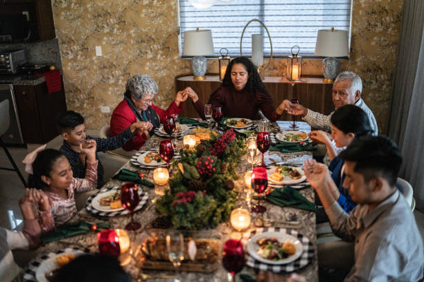 Multi-generational Christian family holding hands in prayer around a dinner table, strengthening family bonds, passing down faith, and fostering unity through shared meals and biblical values. Multi-generational Christian family holding hands in prayer around a dinner table, strengthening family bonds, passing down faith, and fostering unity through shared meals and biblical values.