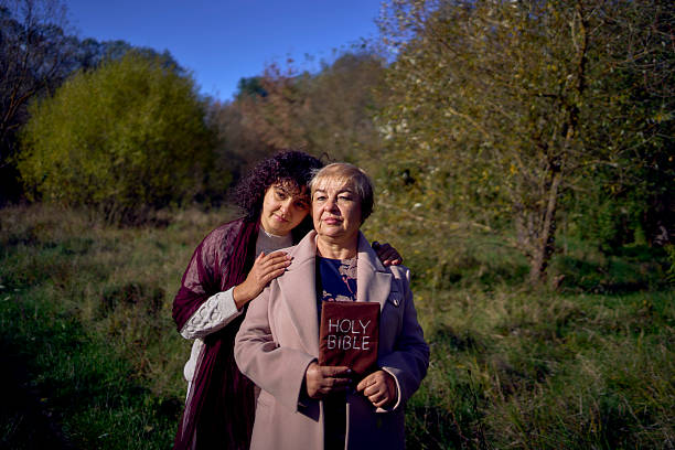 Christian mother and adult daughter standing together outdoors holding a Bible, symbolizing faith, spiritual guidance, God's presence, generational faith, and finding peace through a relationship with Christ.