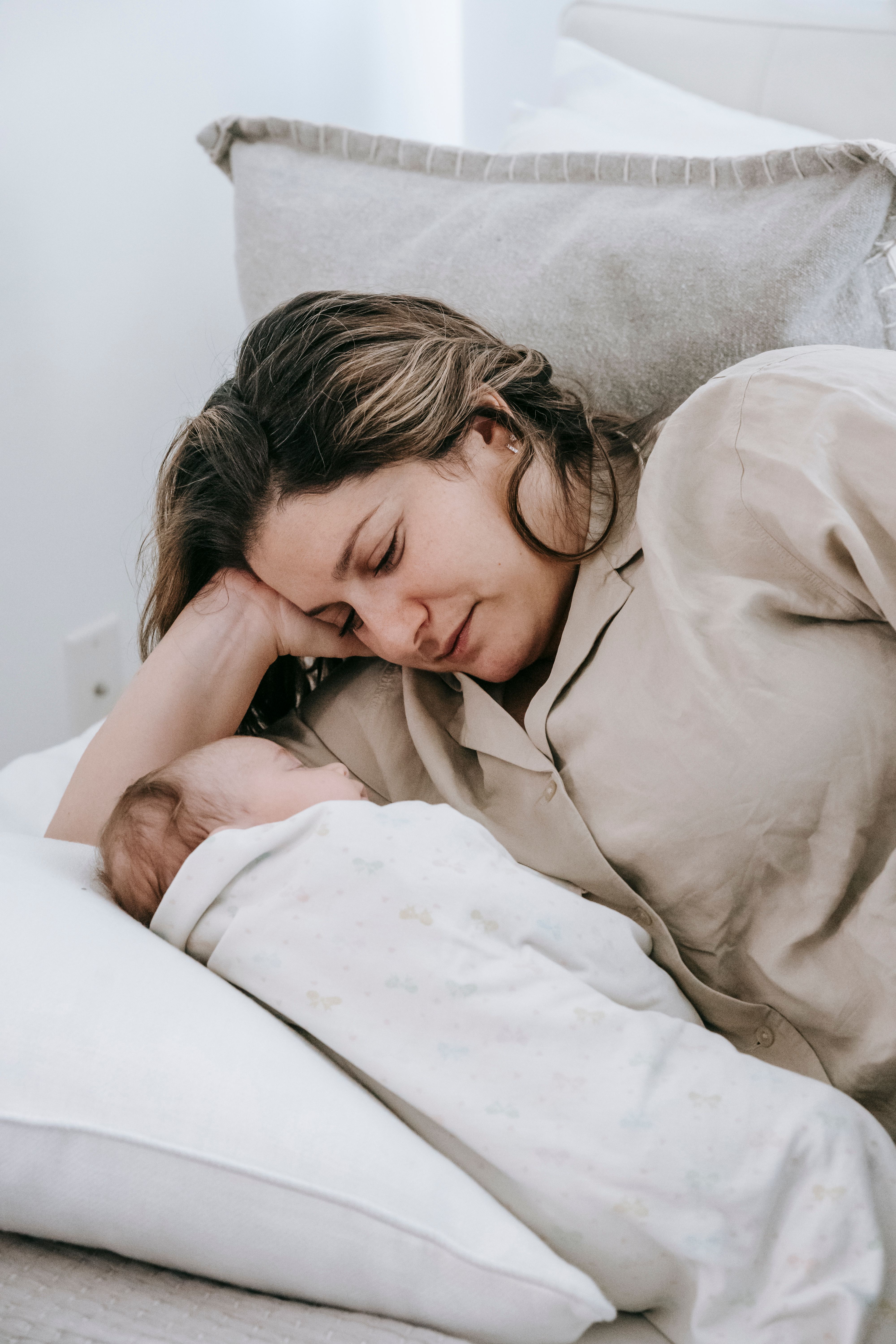 Tired mother resting peacefully beside her sleeping baby in bed, illustrating the importance of rest for mothers and the need to pause, recharge, and trust God while caring for a family.