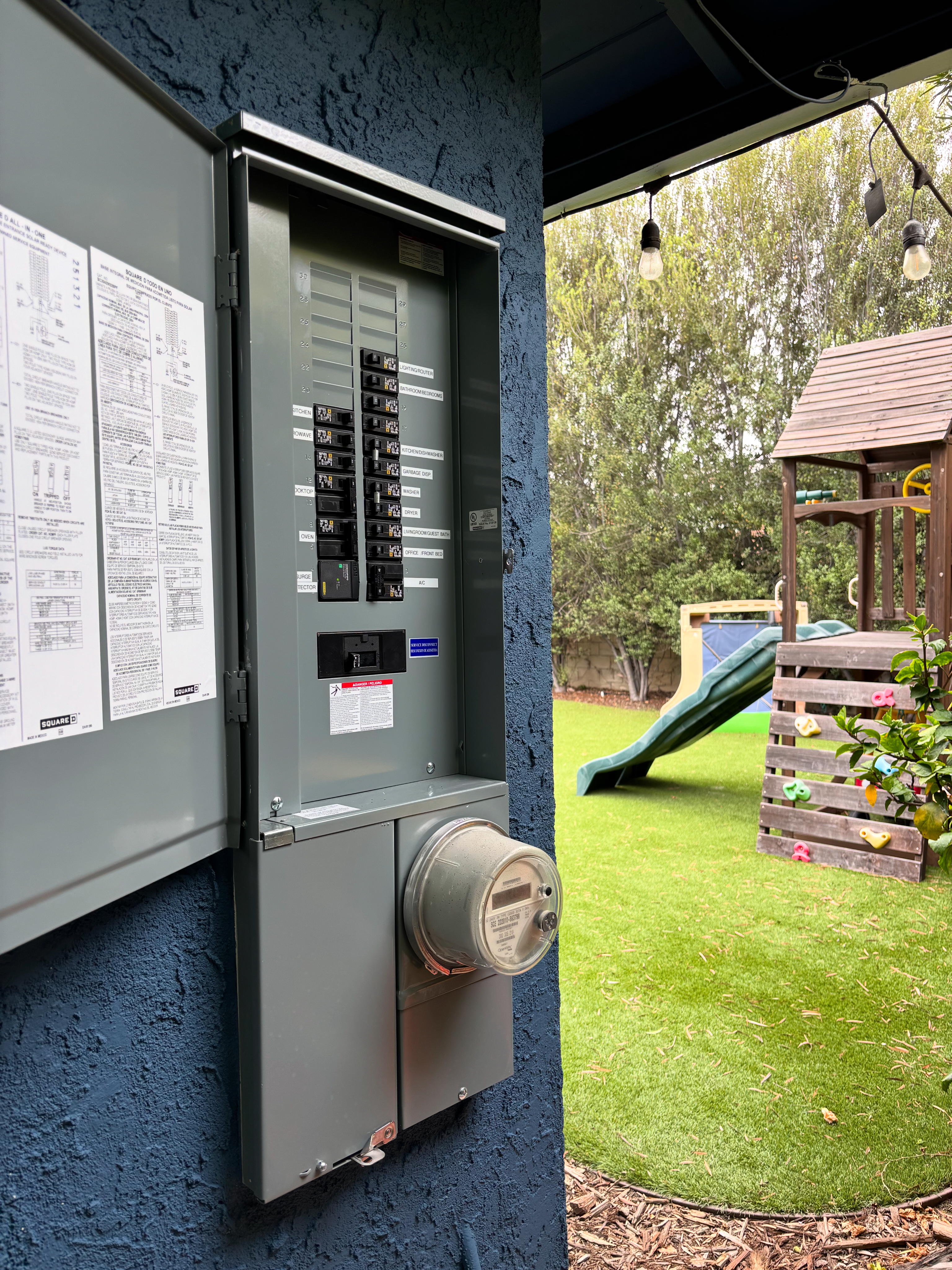 A licensed electrician installs a new residential electrical panel inside an Orange County, CA home, with circuit breakers neatly organized and labeled inside an open metal panel box. The surrounding wall shows clean wiring routed to code, with adequate clearance space maintained around the unit.
