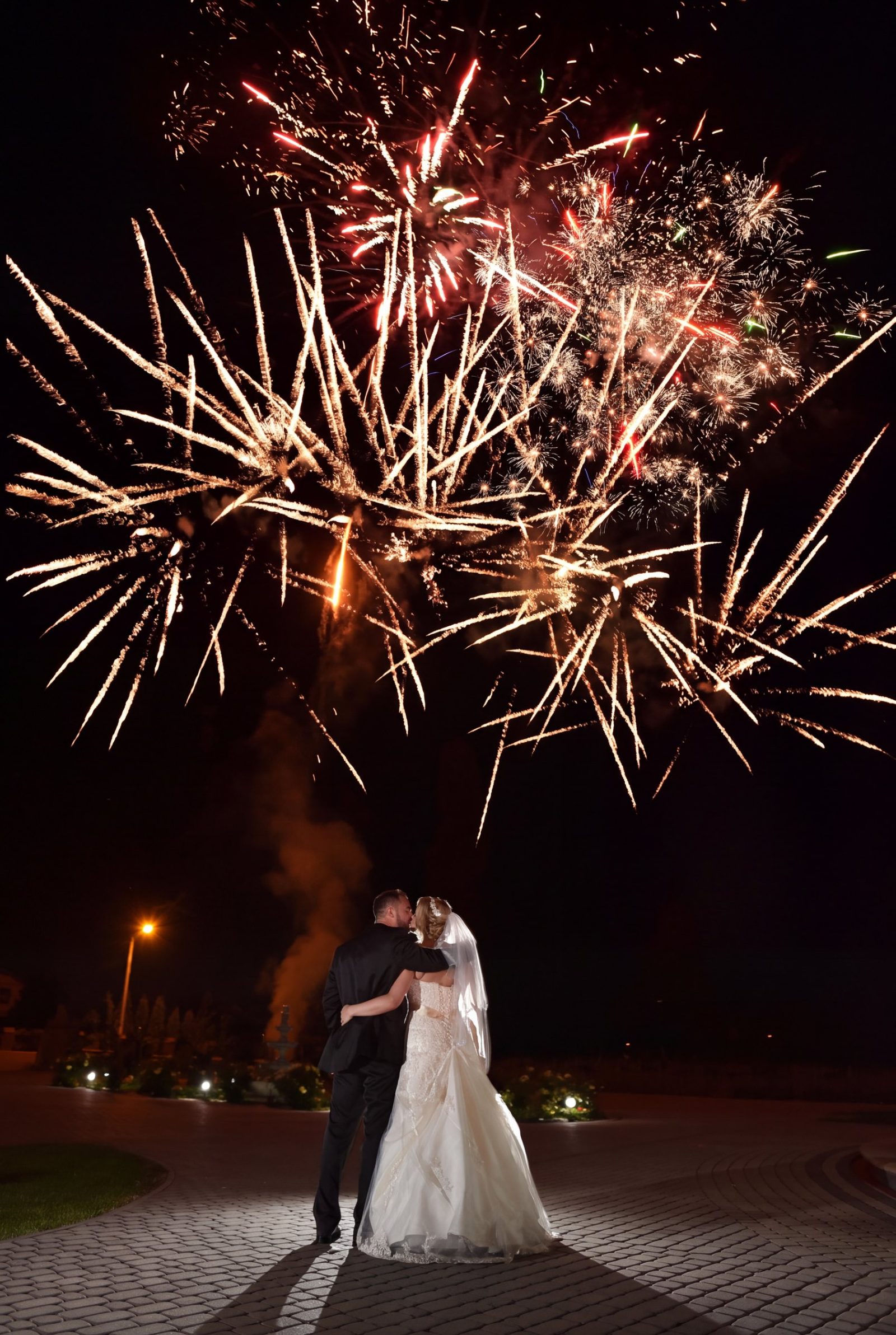 A bride and groom kissing on the beach under fireworks at a real wedding