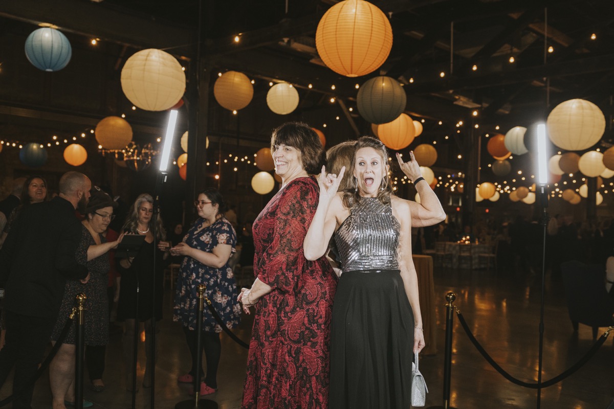 Two guests striking rock poses in front of a photo booth at a lantern-lit barn event