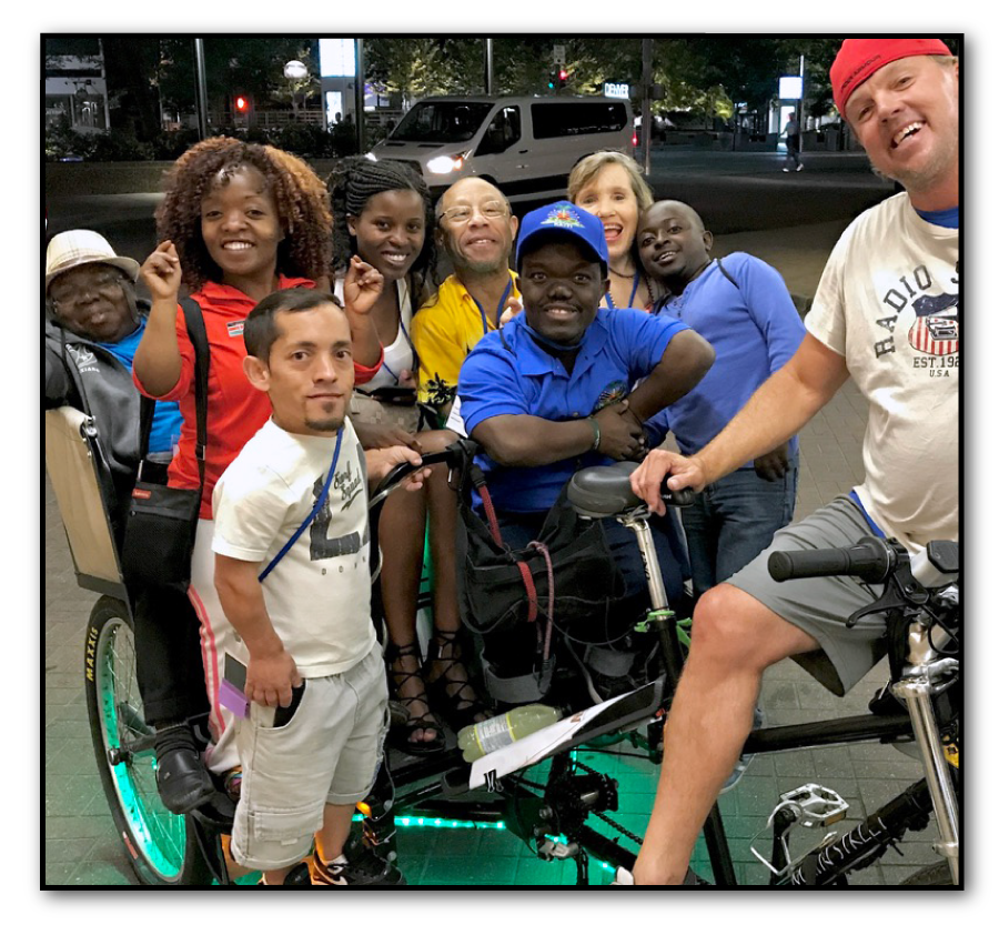 Group of African little people riding together on a community bicycle, symbolizing unity and mobility.