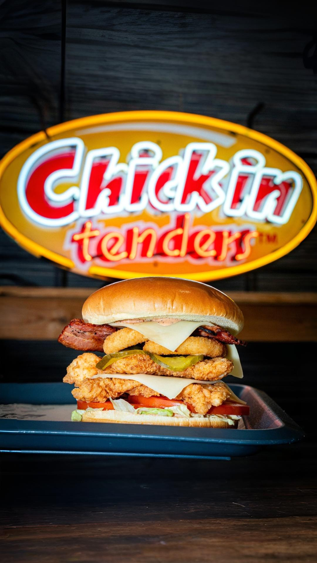 Stacked fried chicken burger in front of Chick-in Tenders sign