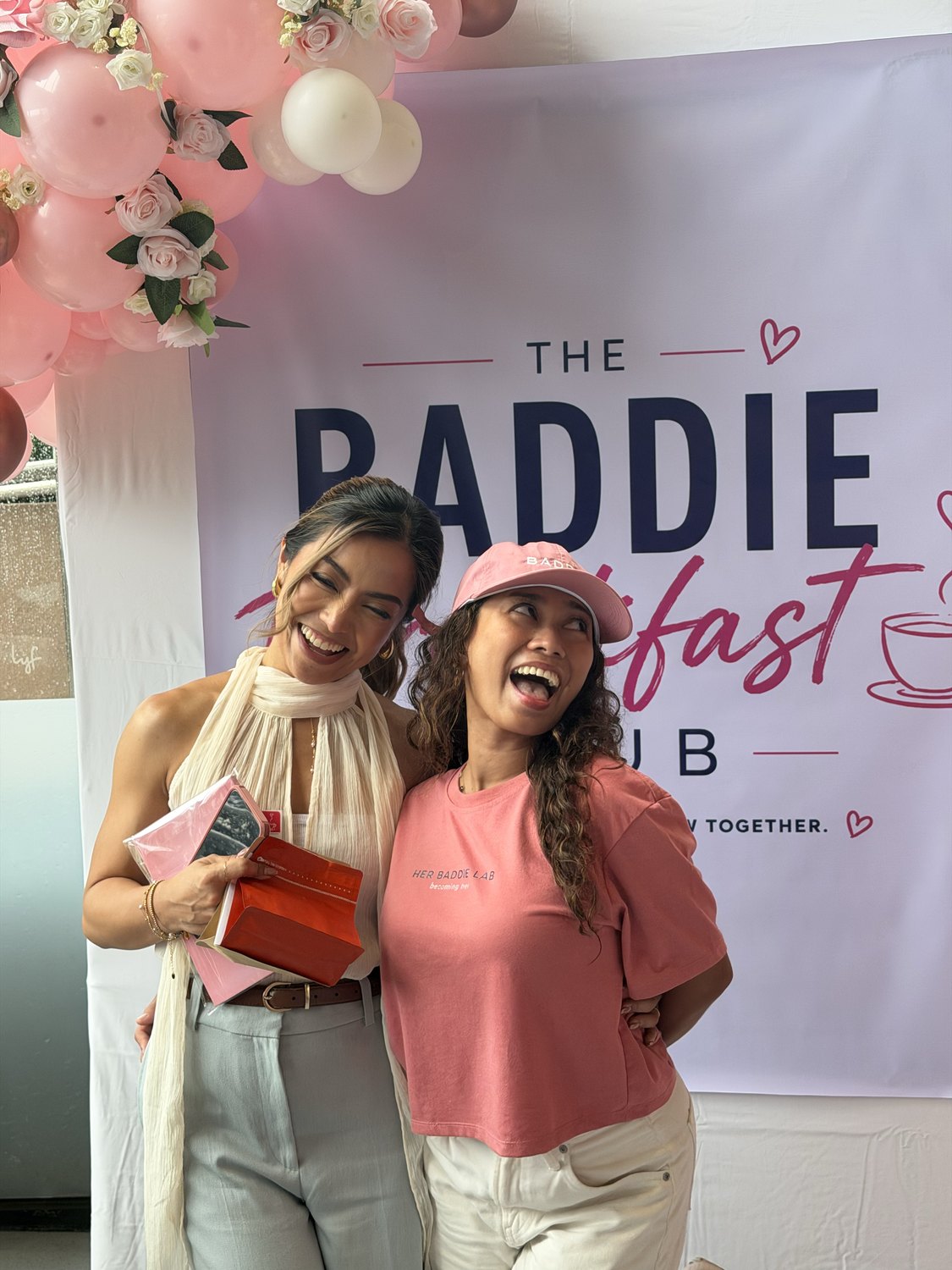 Two women laughing in front of the Baddie Breakfast Club backdrop