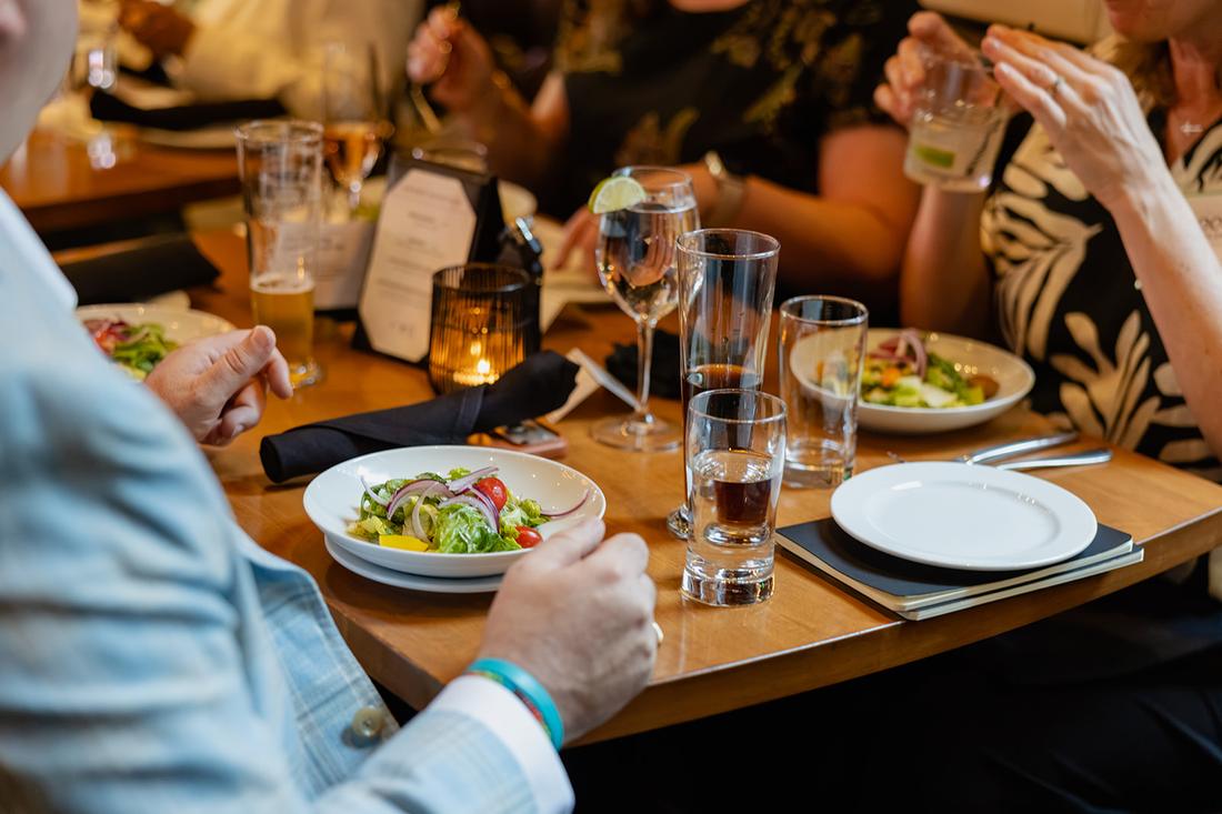 Guests mid-conversation over the salad course, hands raised, glasses and place cards on the table.