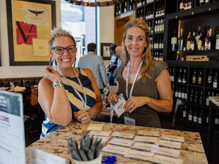 Two guests at the welcome table writing name tags beside rows of printed place cards.