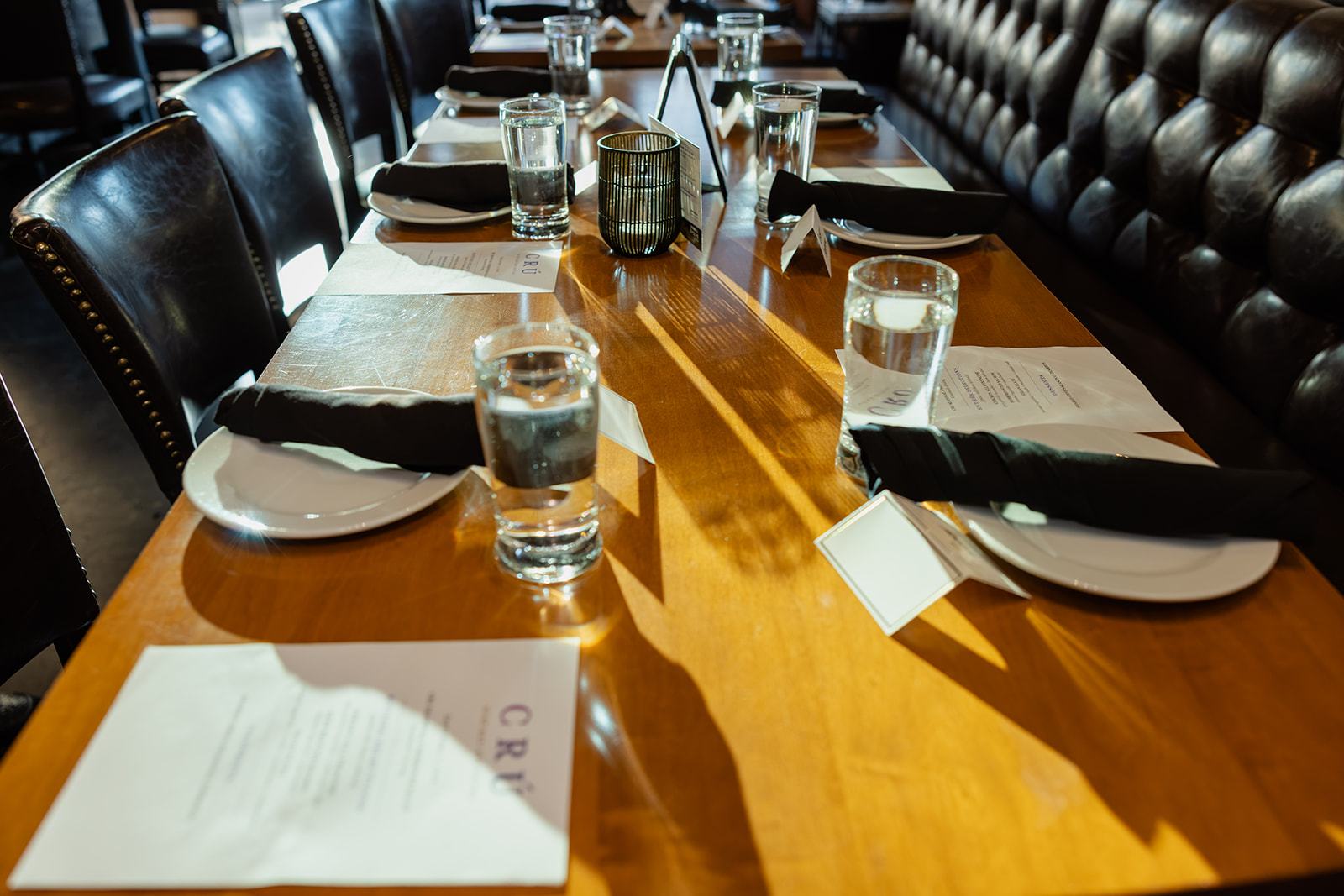 One long dinner table at CRU Atlanta, set with place cards and menus, chairs down one side and a leather bench down the other.