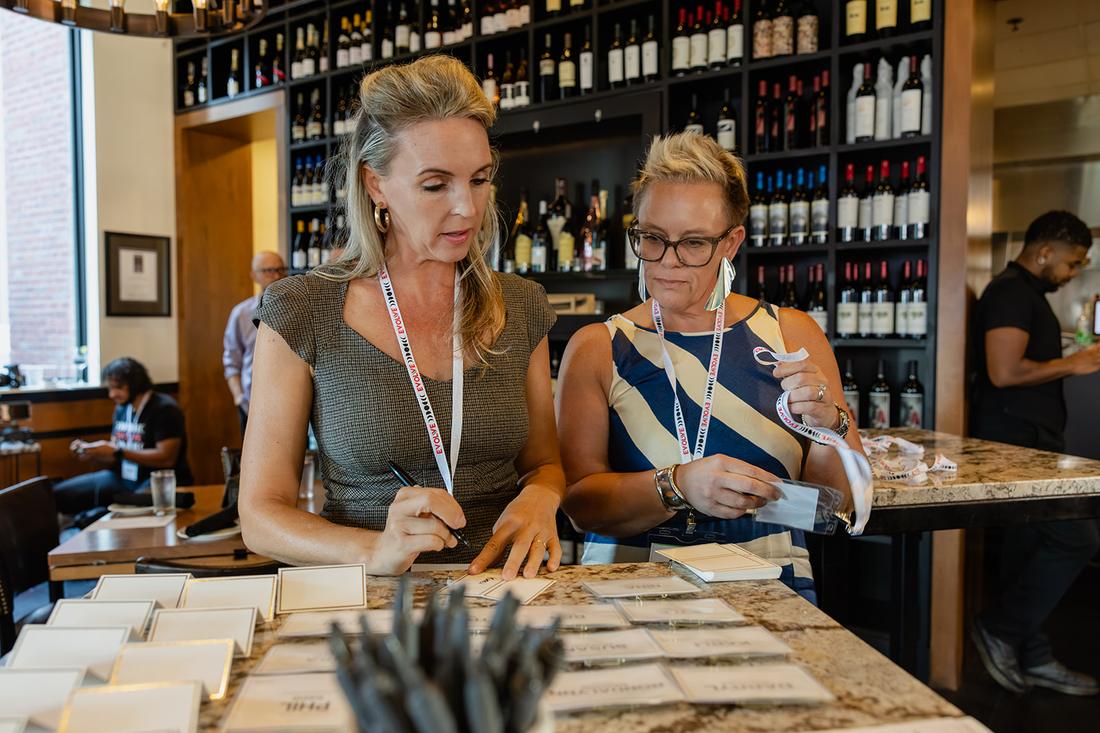 Two hosts at the welcome table, laying out printed place cards and name tags before the doors open.