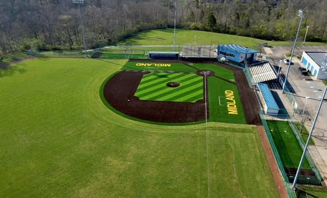 An aerial view of a green baseball field with a brown infield and yellow 'MIDLAND' text on the outfield grass.