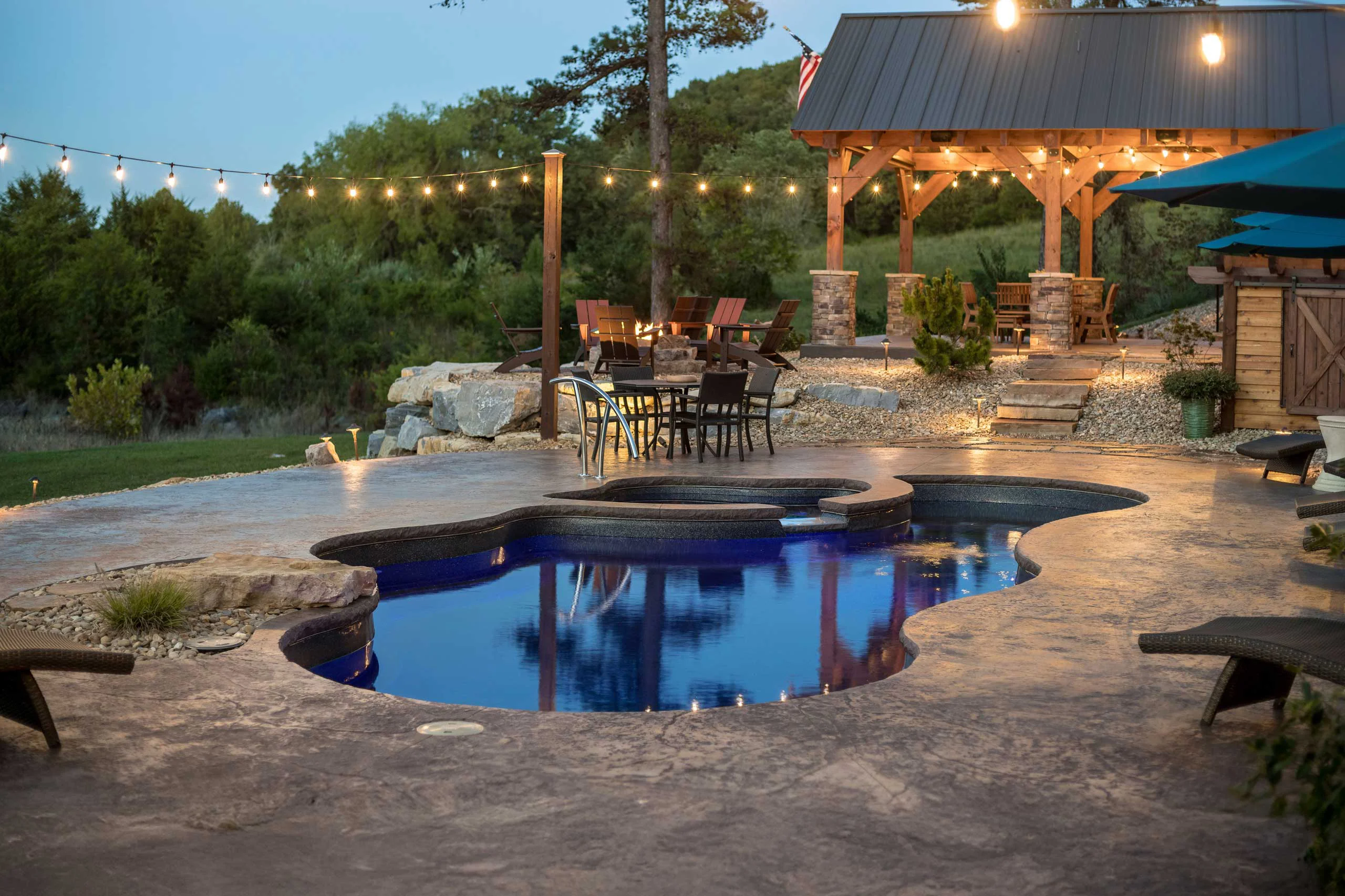 A patio, pool, and outdoor kitchen under a wooden pergola installed by Bollman Landscape A patio, pool, and outdoor kitchen under a wooden pergola installed by Bollman Landscape