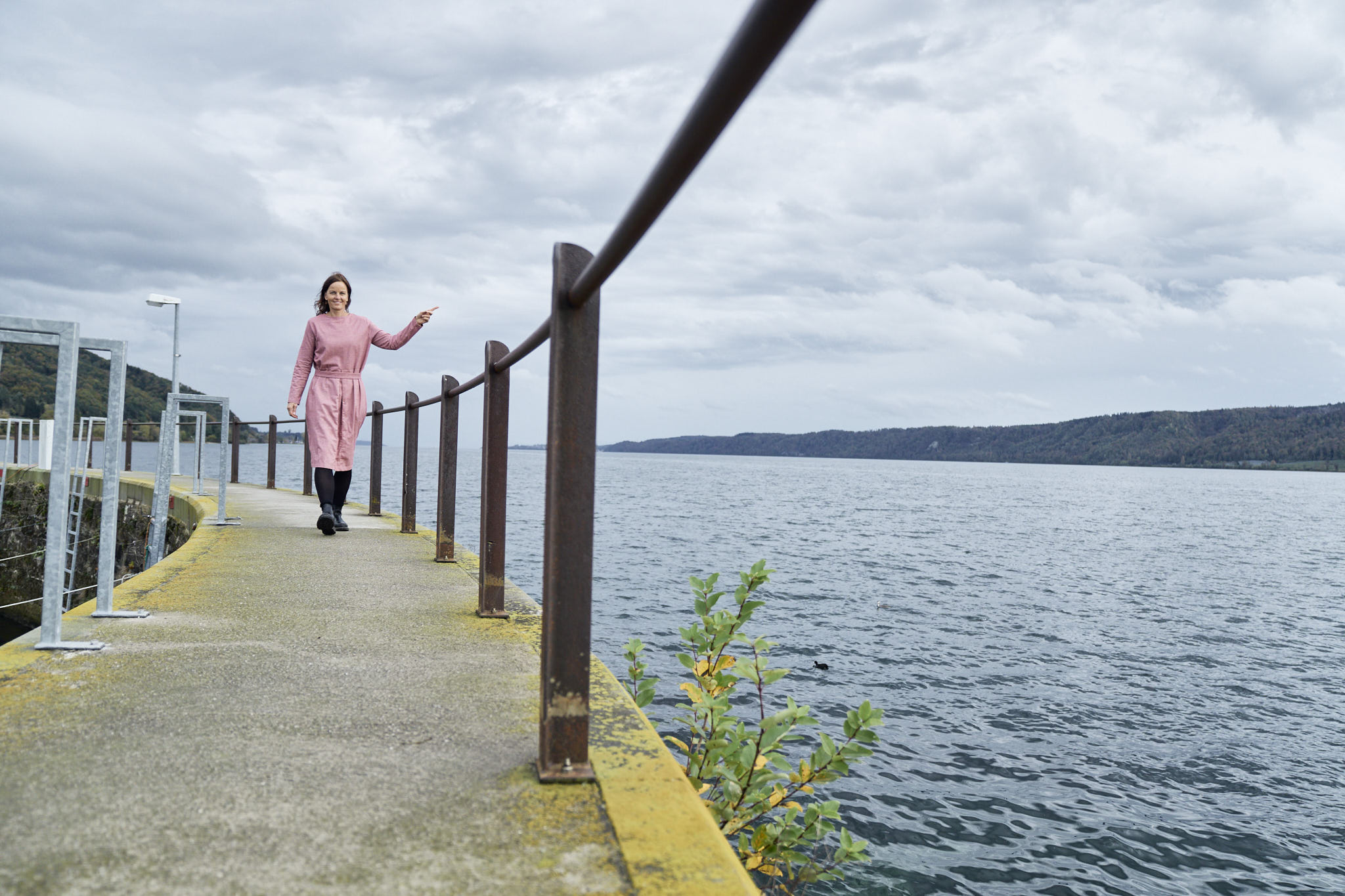 Barbara Kittel-Holmgren geht im rosa Mantel auf einem Steg am Bodenseeufer entlang