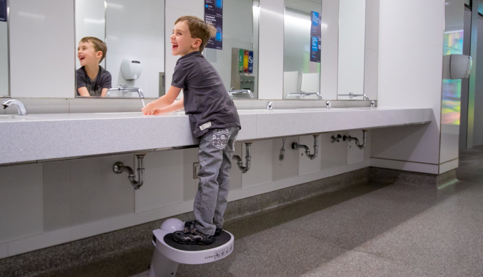 A boy laughing on a Klimbo K01 at a Montréal-Trudeau airport restroom sink