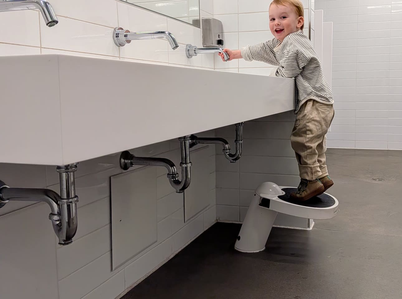 Child using a Klimbo step stool at a public washroom sink