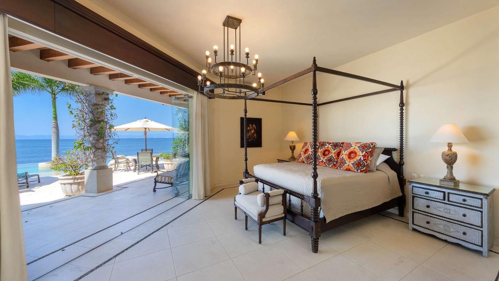 Four-poster bedroom suite with floor-to-ceiling glass opening to ocean terrace